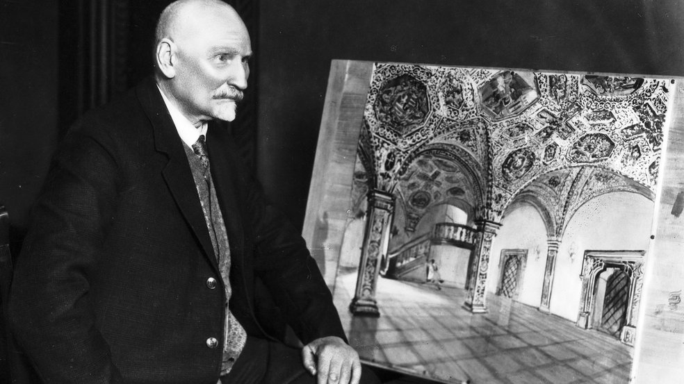 archiwalne czarno białe zdjęcie przestawiające starszego mężczyzne z łysą głową i szpiczastą bródkaubrany w garnitur siedzi bokiem obok niego obraz przedstawiający sale w ratuszu poznańskim