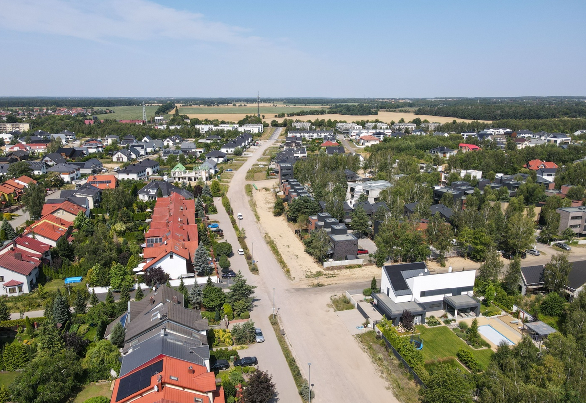 widok z lotu ptaka na zabudowę domów szeregowych i jednorodzinnych wzdłuż drogi, między budynkami rosną drzewa - grafika artykułu