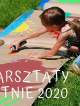 Dziwczyna maluje słońce i zwierzęta na szrym papierze rozłozonym na trawie.