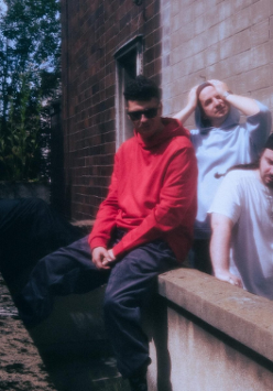 Czterech mężczyzn siedzi i stoi przy murku obok ściany budynku.