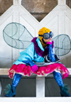 Kobieta przebrana w kolorowe ciuchy za muchę siedząca na białej ławie.