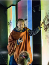 Dzieci z przewodnikiem w stroju z epoki średniowiecza przy interaktywnej mapie.