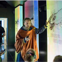 Dzieci z przewodnikiem w stroju z epoki średniowiecza przy interaktywnej mapie.