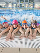 Rozesmiane dzieci w basenie, nogi w wodzie a ręce na brzegu.