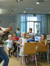 Dzieci siedza na krzesłach przy stolikach z laptopami. W sali sa instruktorzy.