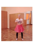 Kobieta w stroju baletnicy, w różowej spódnicy, jasnej koszulce i czarnych getrach, w sali ze ścianą z luster.