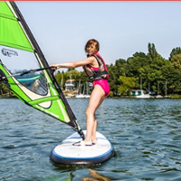 Dziewczyna w rózowym stroju kapielowym na desce windsurfingowej na jeziorze. Zielony żaiel.
