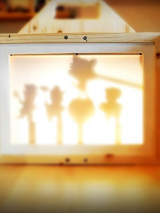 Drewniany teatr obrazkowy Kamishibai. W centralnym punkcie widoczne cienie, zarysy lalek.