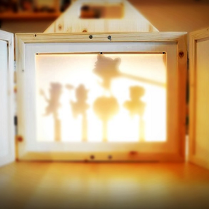 Drewniany teatr obrazkowy Kamishibai. W centralnym punkcie widoczne cienie, zarysy lalek.