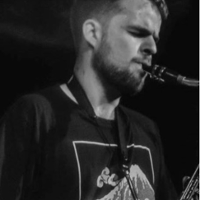 Czarno biała fotografia przedstawia profil młodego mężczyzny grającego na saksofonie