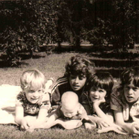 Fotografia przedstawiająca pięcioro dzieci leżące na kocu w sadzie.
