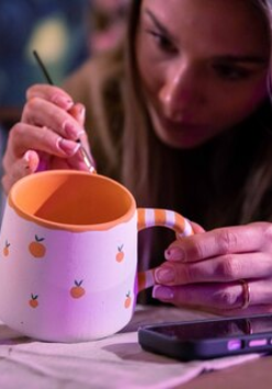 Malowanie ceramicznego kubka farbą przy pomocy pędzelka.