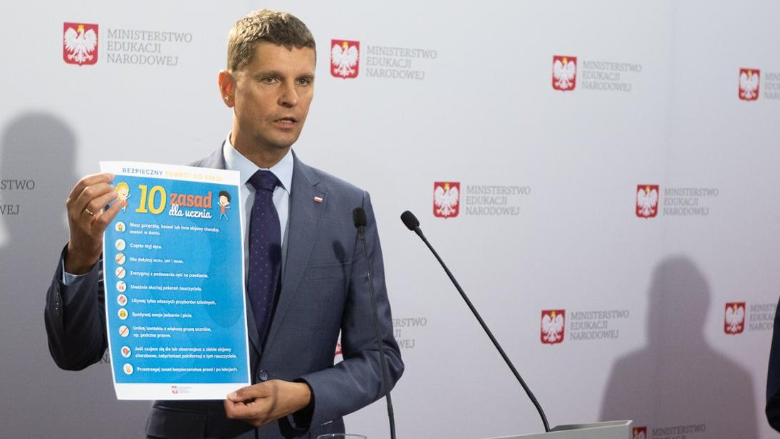 na zdjęciu widać Ministra Edukacji Narodowej trzymającego plakat "10 zasad dla ucznia"
