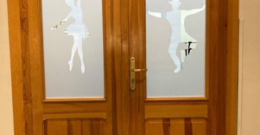 zdjęcie przedstawia drzwi wejściowe do sali tanecznej, na których wycięci w mlecznej szybie są: tancerz i tancerka