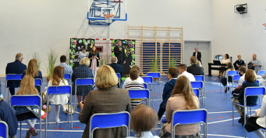 Zdjęcie przedstawia wiceprezydenta Wiśniewskiego w sali gimnastycznej i słuchających go uczniów i nauczycieli.