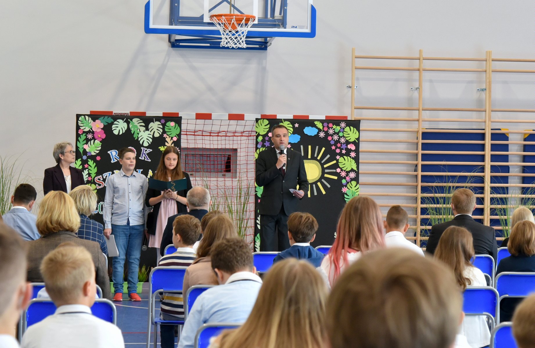 Zdjęcie przedstawia wiceprezydenta Wiśniewskiego z mikrofonem oraz słuchających go uczniów na sali gimnastycznej. - grafika artykułu
