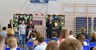 Zdjęcie przedstawia wiceprezydenta Wiśniewskiego z mikrofonem oraz słuchających go uczniów na sali gimnastycznej.