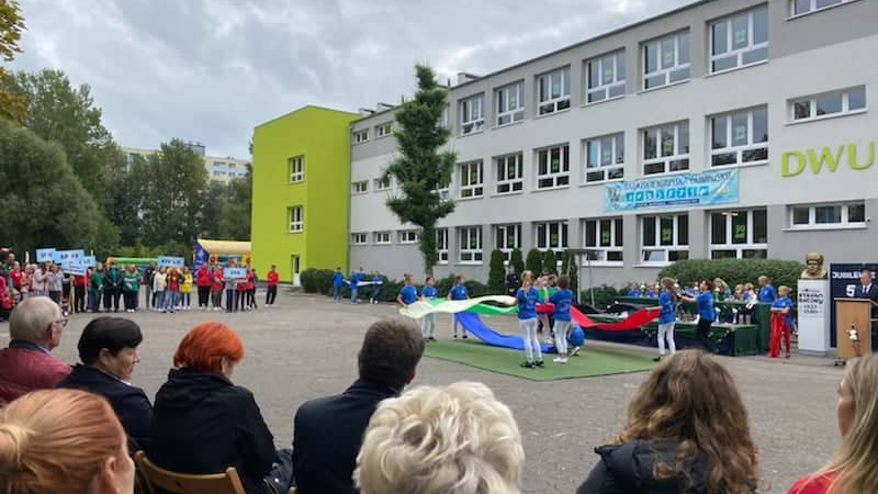 zdjęcie przestawia uczniów stojących przed szkołą, będących w trakcie ceremoniału olimpijskiego