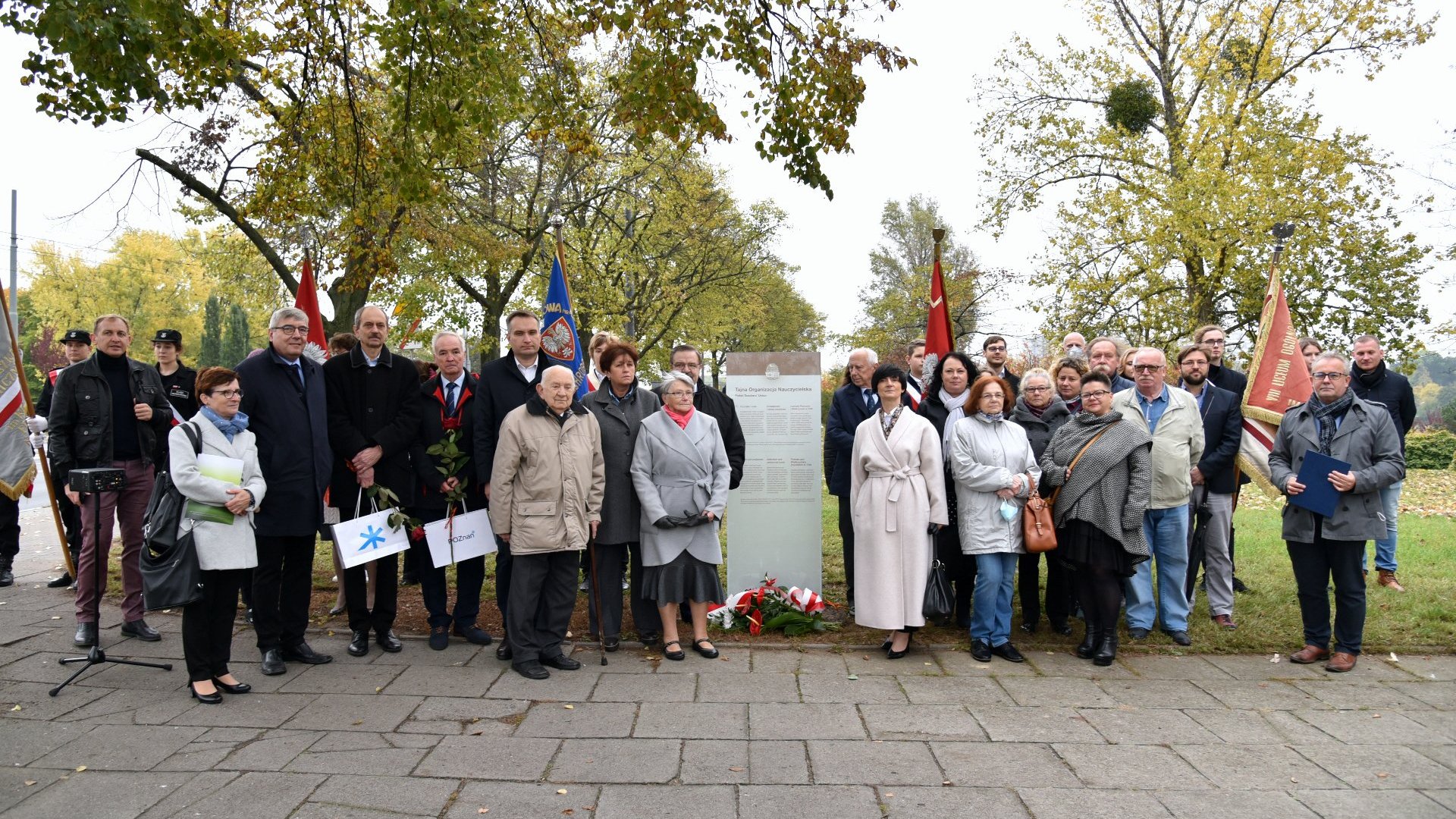 Zdjęcie przedstawia uczestników uroczystości na zdjęciu grupowym przy tablicy. - grafika artykułu