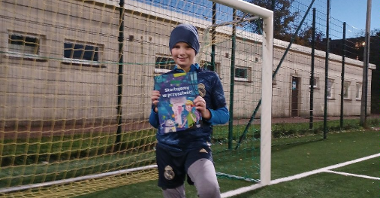 zdjęcie przedstawia chłopca z książką i piłką na boisku