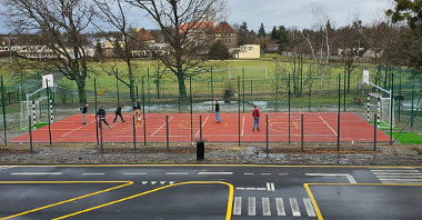 Zdjęcie przedstawia szkolne boisko, na którym uczniowie grają w piłkę.