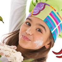 Dziewczynka ubrudzona mąką, trzyma surowe ciasto w ręce, na głowie ma kolorową czapkę kucharską. Obok rysunki czosnku, cytryny, liści, doniczki z ziołami i młynku do pieprzu.
