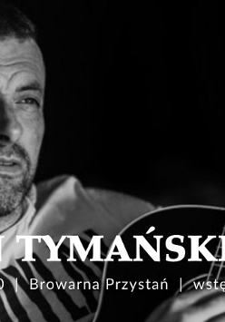 Czarno-białe, bliskie ujęcie mężczyzny z krótkim zarostem, który patrzy w bok z lekkim uśmiechem. W dolnej części kadru widoczny jest gryf i fragment korpusu gitary akustycznej trzymanej przez artystę. Tło jest ciemne i nieostre. Na froncie napisy, będące szczegółami wydarzenia, które są zawarte w artykule.