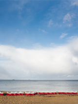 Plaża - obraz niebo, morze i piaszczysta plaża.Na plaży biało-czerwone parawany.