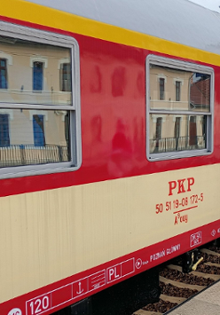 Biało-beżowy wagon starego składu pociagow PKP. Ma duże okna. Stoi na peronie.