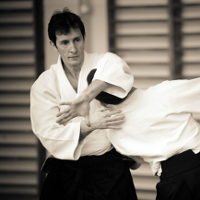 Zdjęcie przedstawia sensei aikido, wykonującego chwyt na głowie partnera treningowego.