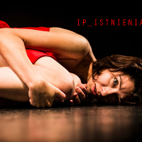 Zdjęcie ze spektaklu - kobieta w czerwonej sukience leży skulona na podłodze.
