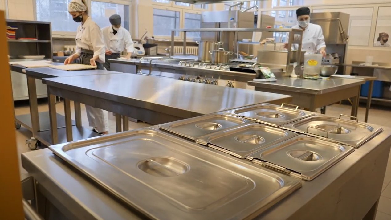 Szkolna pracownia wyglądająca jak kuchnia w restauracji. Na zdjęciu widać metalowe stoły, przy których pracuje trójka uczniów. - grafika artykułu