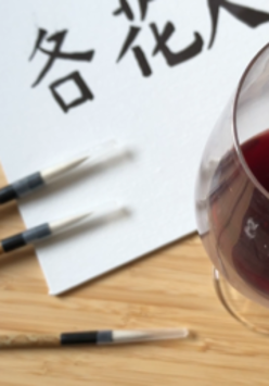 Kartka papieru a na niej chińska kaligrafia, obok kieliszek z czerwonym napojem.