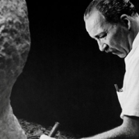 Na czarno-białym zdjęciu artysta rzeźbiący w kamieniu.