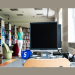 Na zdjęciu pomieszczenie biblioteczne. Na pierwszym planie stolik z komputerem, w tle regały z książkami.