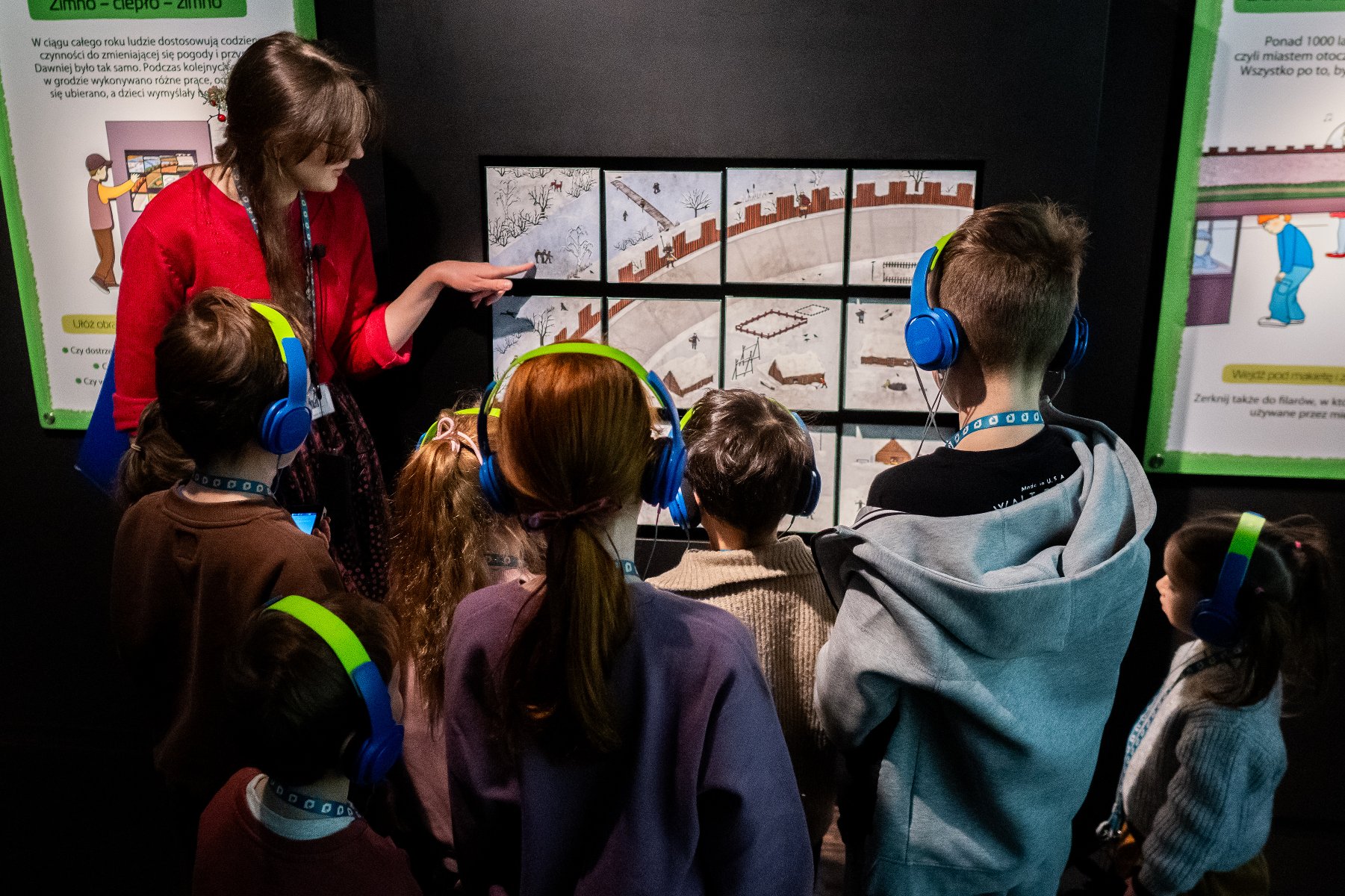 Zdjęcie przedstawia grupę dzieci stojących przy muzealnej ekspozycji obrazującej dawny gród.