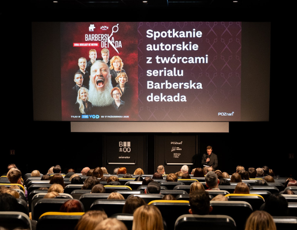 Zdjęcie przedstawia salę kinową. Na krzesłach siedzą młodzi ludzi, a na ekranie jest informacja o serialu i spotkaniu autorskim.