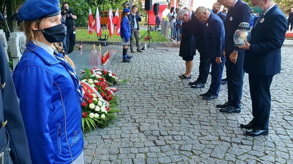 Cmentarz na Westerplatte. Po lewej pomnik, po prawej samorządowcy w uroczystym pokłonie, tuż po złożeniu kwiatów - grafika artykułu