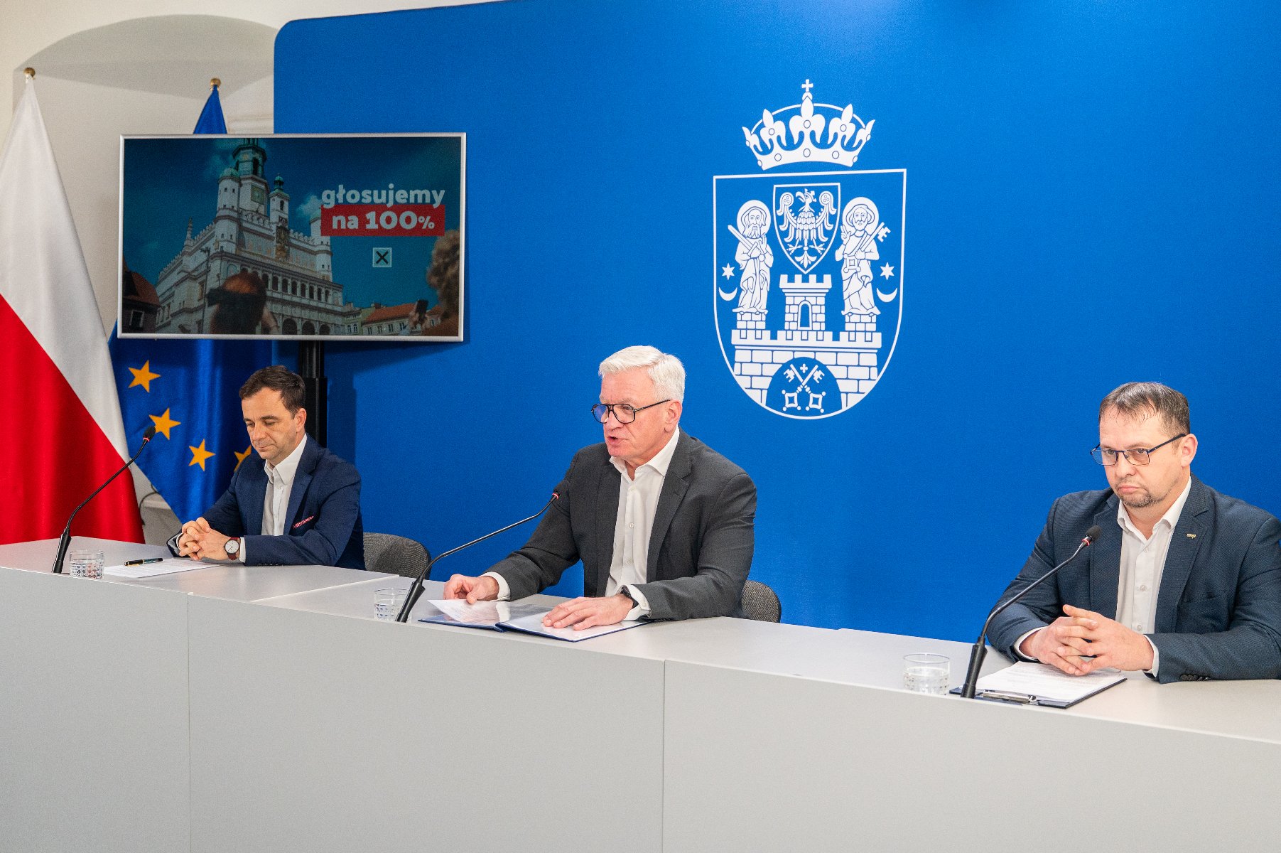 Prawo do wyboru Prezydenta Rzeczypospolitej Polskiej ma każdy obywatel naszego kraju Na zdjęciu trzej mężczyźni za stołem konferencyjnym, w tle ekran z zachętą do głosowania