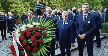 Na pierwszym planie strażnik miejski trzyma wiązankę kwiatów, za nim samorządowcy, w tym Jacek Jaśkowiak, prezydent Poznania