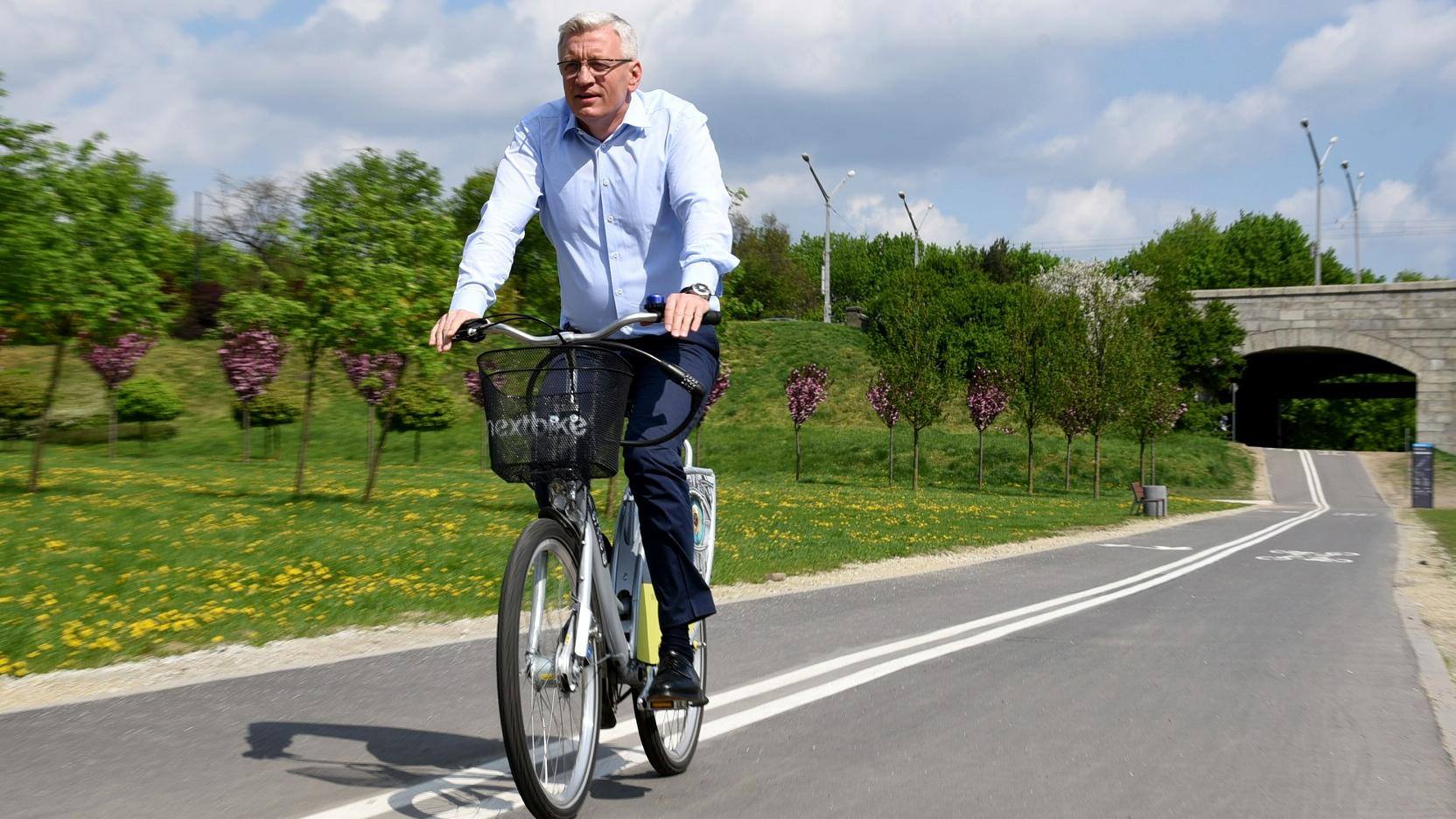 Jacek Jaśkowiak, prezydent Poznania na rowerze. W tle wiadukt i zieleń. - grafika artykułu
