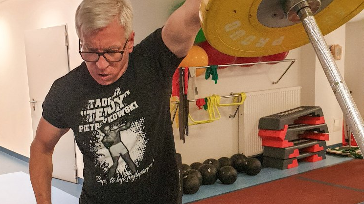 Jacek Jaśkowiak w sportowych ubraniach wyciska sztangę na siłowni. - grafika artykułu