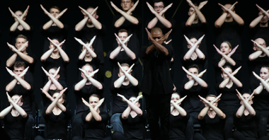 Na zdjęciu grupa tancerzy, wszyscy mają ręce złożone w znak X