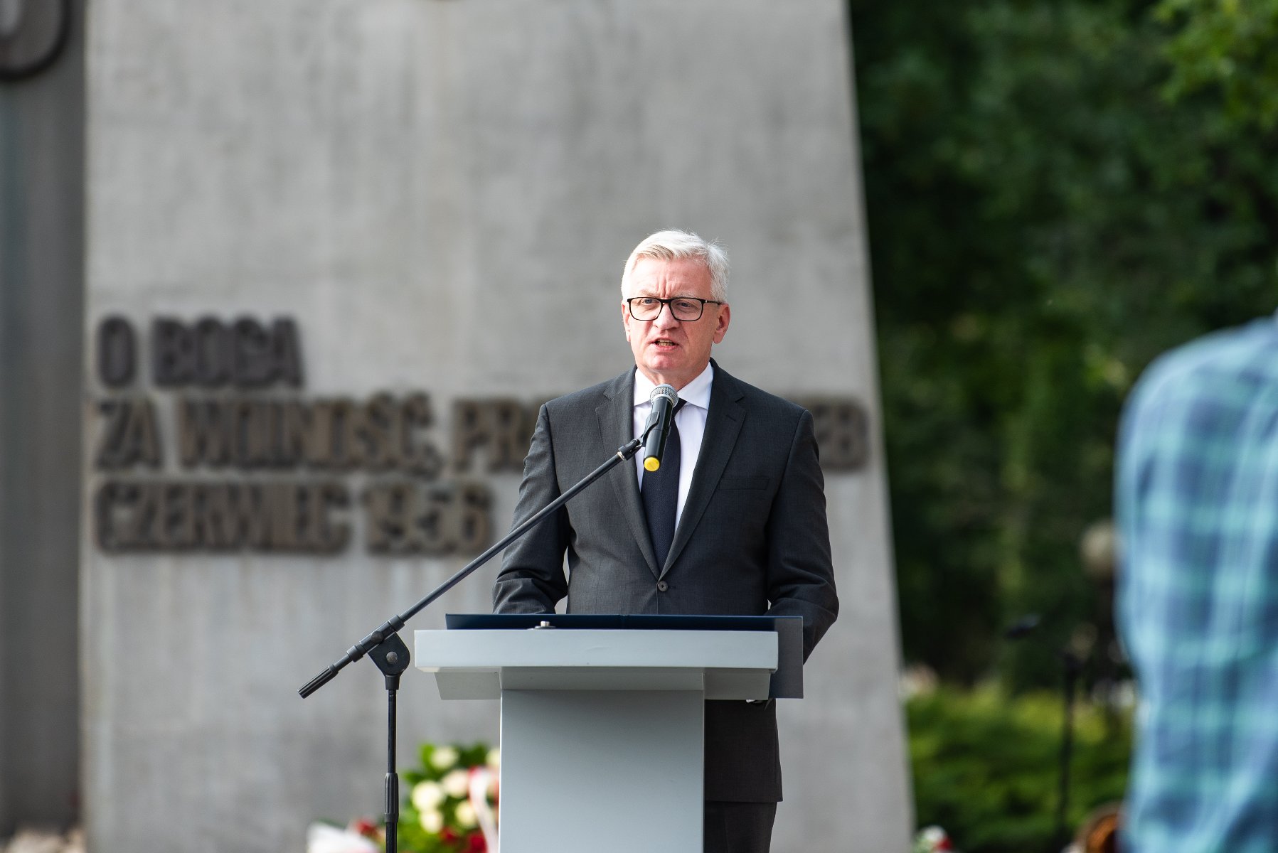 Na zdjęciu Jacek Jaśkowiak, prezydent Poznania, przy mikrofonie, w tle Pomnik Poznańskiego Czerwca - grafika artykułu
