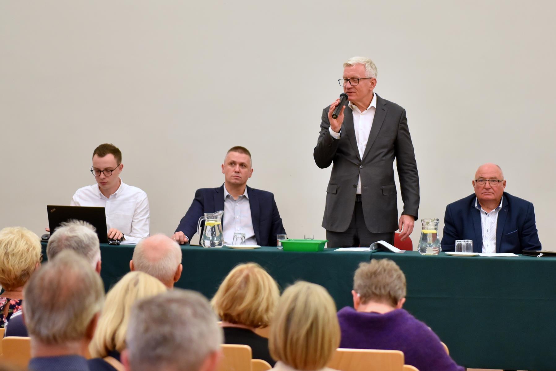 Na zdjęciu Jacek Jaśkowiak trzymający mikrofon, obok niego siedzi 3 mężczyzn, na pierwszym planie publiczność - grafika artykułu