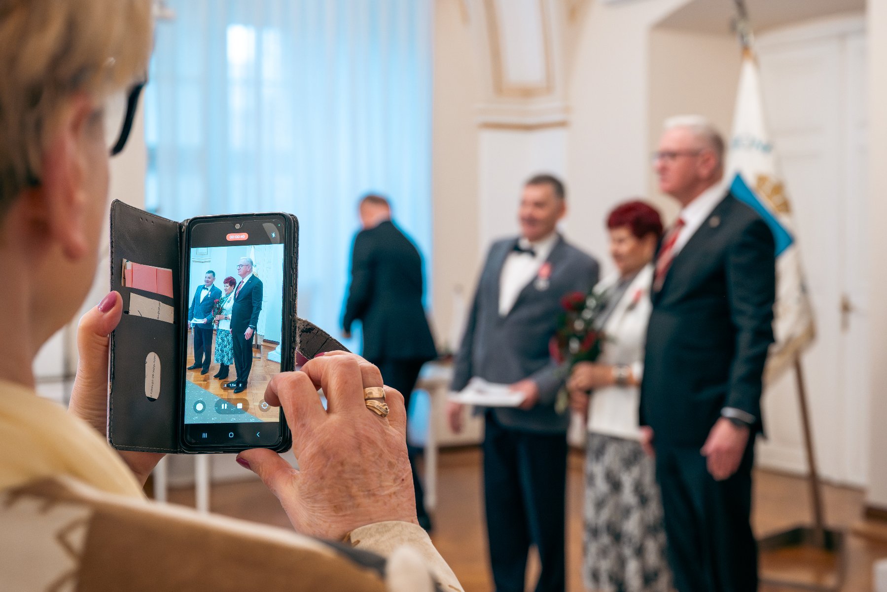 Zdjęcie przedstawia prezydenta ściskającego rękę kobiecie. Obok stoi mężczyzna.
