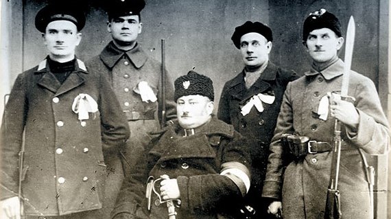 Czarno białe zdjęcie pięciu mężczyzn z bronią i wstążkami powstańczymi.