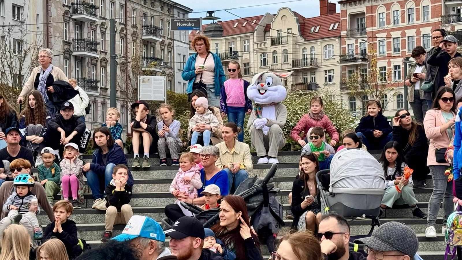 Osoby siedzące na schodach i oglądające przedstawienie na płycie Rynku Łazarskiego.