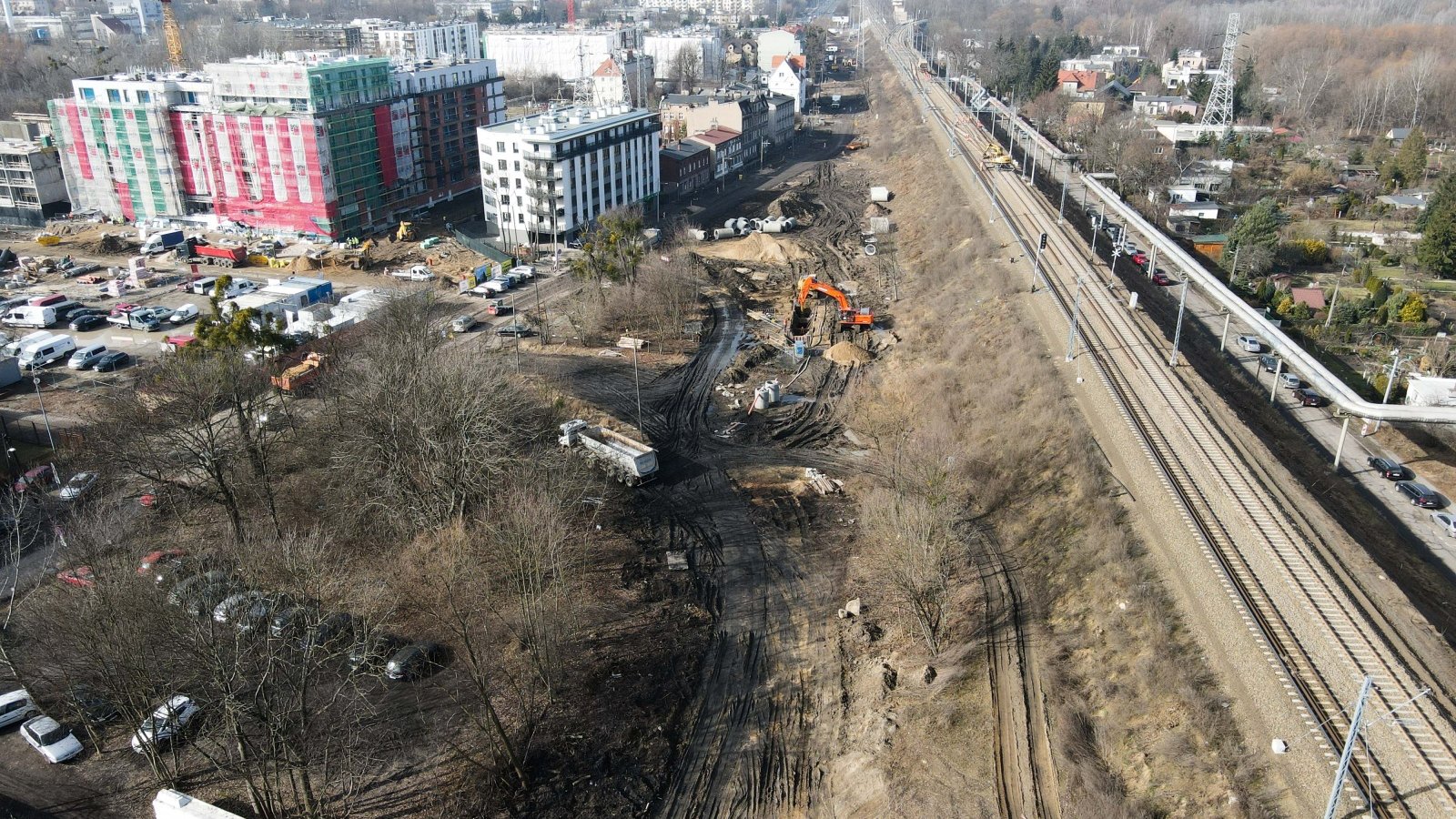 Widok z góry. Po prawej tory kolejowe, po lewej bloki i parkingi. Na dole plac budowy.