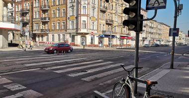 Sygnalizacja świetlna przy ul. Niegolewskich. Po prawej, obok sygnalizatora zaparkowany rower. Po lewej samochód.